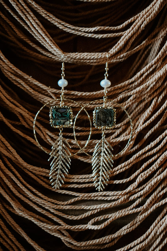 Pair of earrings with green stones and feather designs on a textured brown background