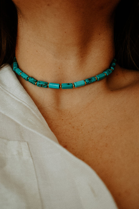 Close-up of a turquoise beaded necklace on a person wearing a white top.